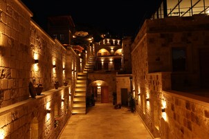 Un estrecho pasillo de piedra con una escalera que conduce a un nivel superior, iluminado por una cálida luz.