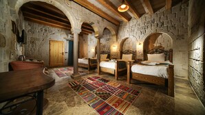 Una habitación rústica con paredes de piedra, vigas de madera y una cama grande con un tapete colorido.