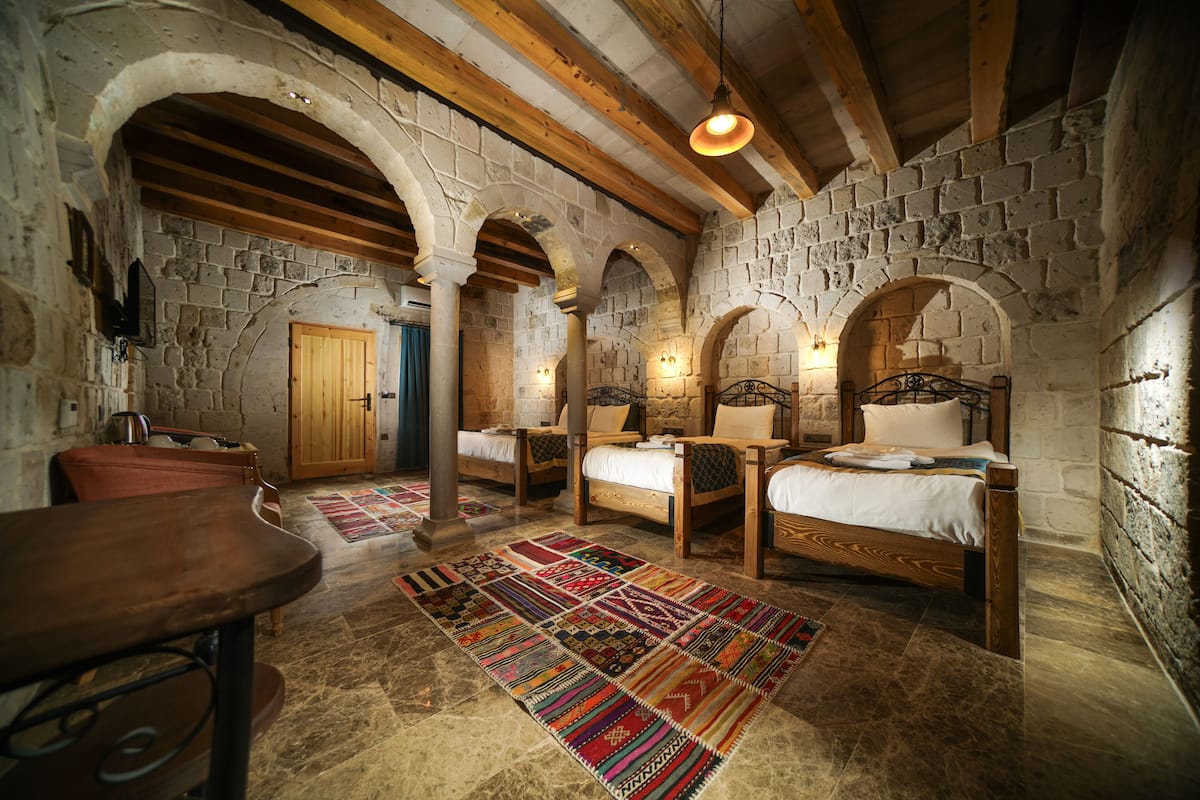 A rustic room with stone walls, wooden beams, and a large bed with a colorful rug.