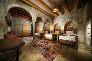 Una habitación rústica con paredes de piedra, vigas de madera y una cama grande con un tapete colorido.