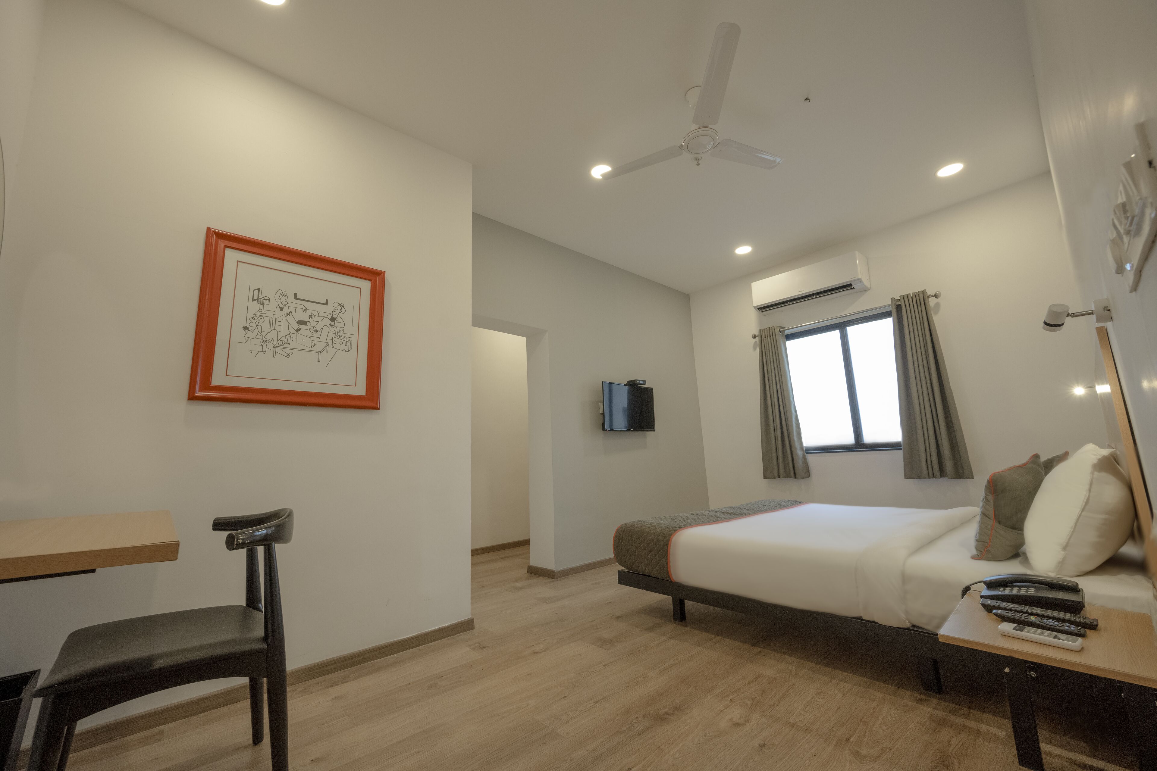 A hotel room with a bed, a desk, a chair, a ceiling fan, a TV, and a window with curtains.