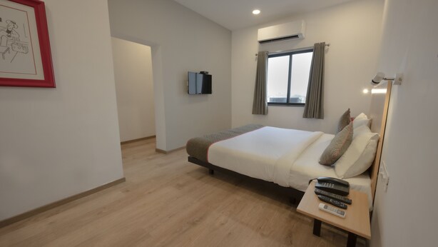 Une chambre à coucher comprenant un lit, une table de chevet avec des télécommandes, un téléviseur fixé au mur et un appareil de climatisation.