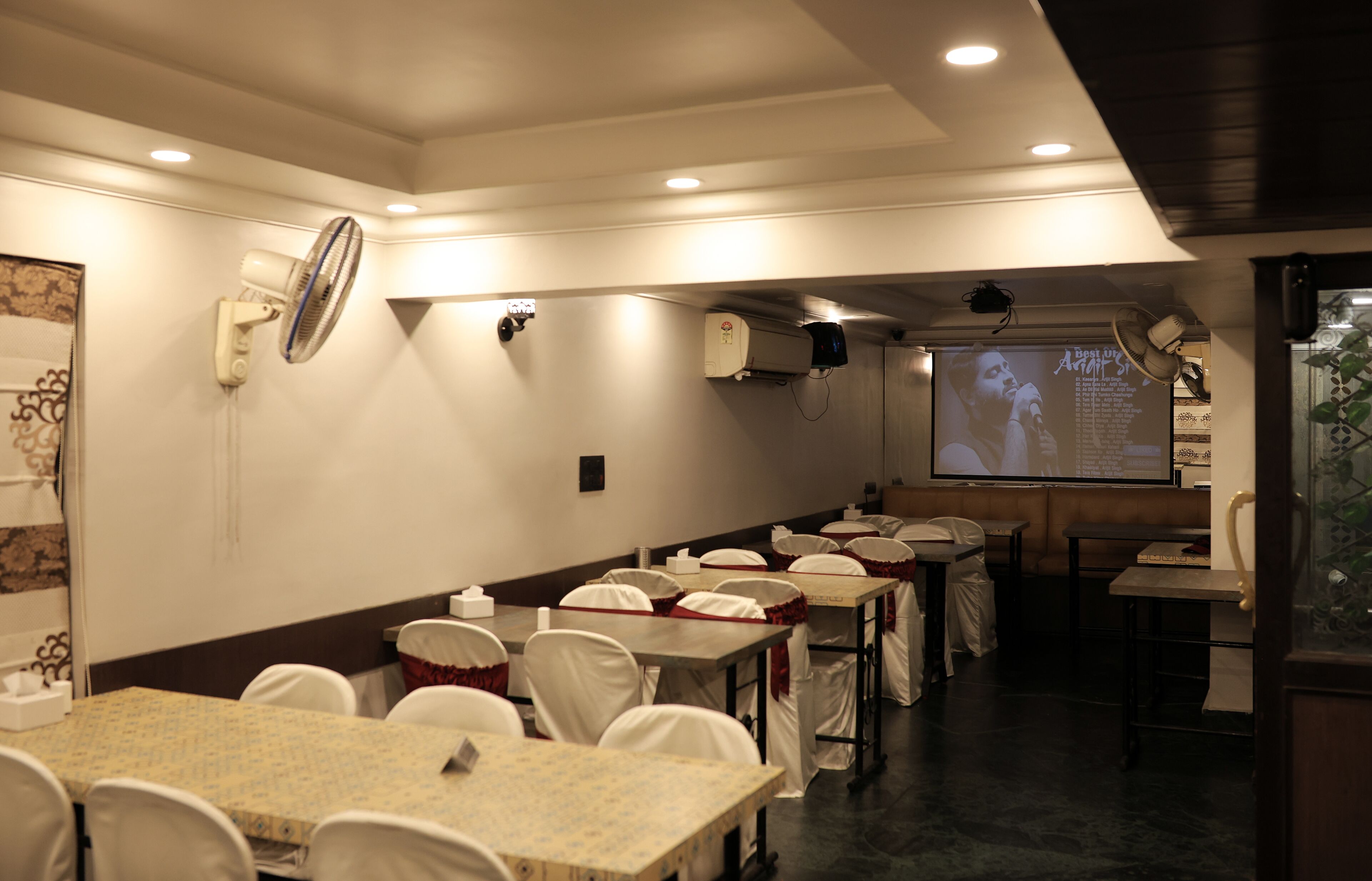 A conference room with tables and chairs, a projector screen, and ceiling fans.