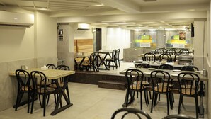 Un restaurant avec plusieurs tables et chaises, un espace cuisine à l’arrière-plan et un appareil de climatisation fixé au mur.