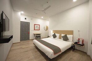 A hotel room with a large bed, a desk, a chair, a ceiling fan, a mirror, and a nightstand with a tray. - Signature Inn (Nagpur)