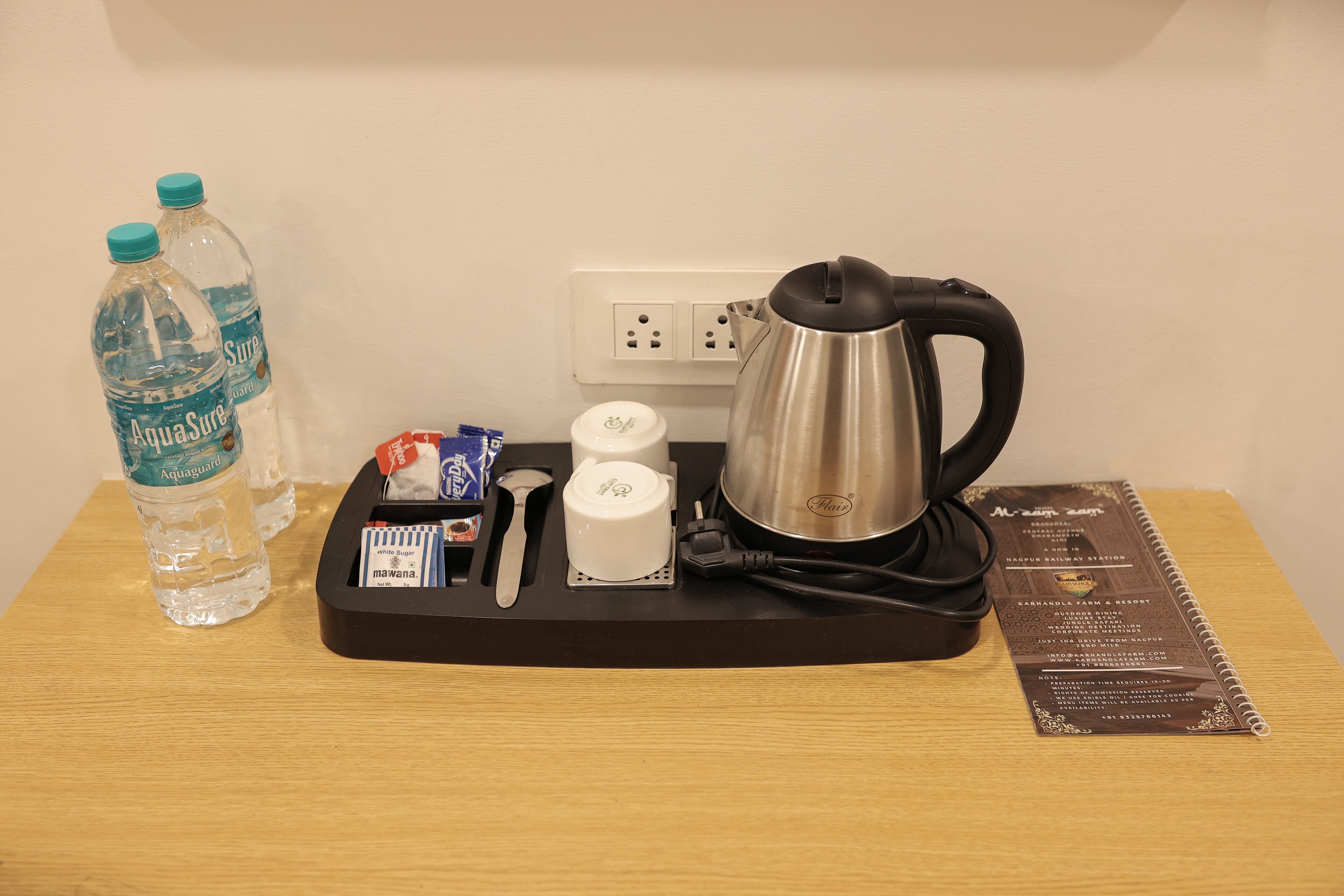 A hotel room's breakfast tray with a kettle, sugar packets, a spoon, and two bottles of water.
