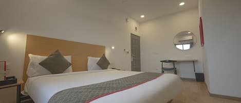 A hotel room with a large bed, a bedside table, a desk, a mirror, and a ceiling fan.