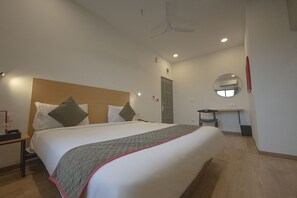 A hotel room with a large bed, a bedside table, a desk, a mirror, and a ceiling fan. - Signature Inn (Nagpur)