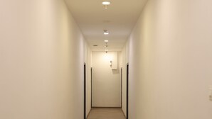 Un couloir étroit et bien éclairé, doté d’un plancher en bois et de murs blancs, qui mène à une porte au fond.