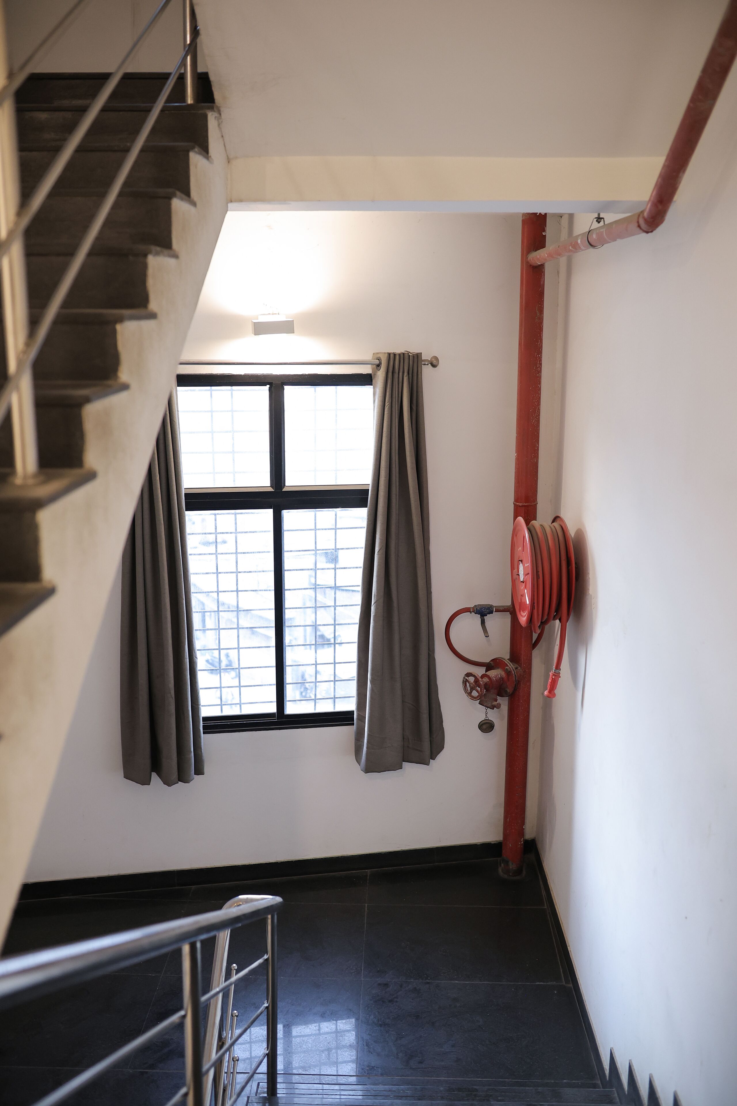 Uma escadaria com janela, carretel de mangueira de combate a incêndio vermelho e corrimão de metal.