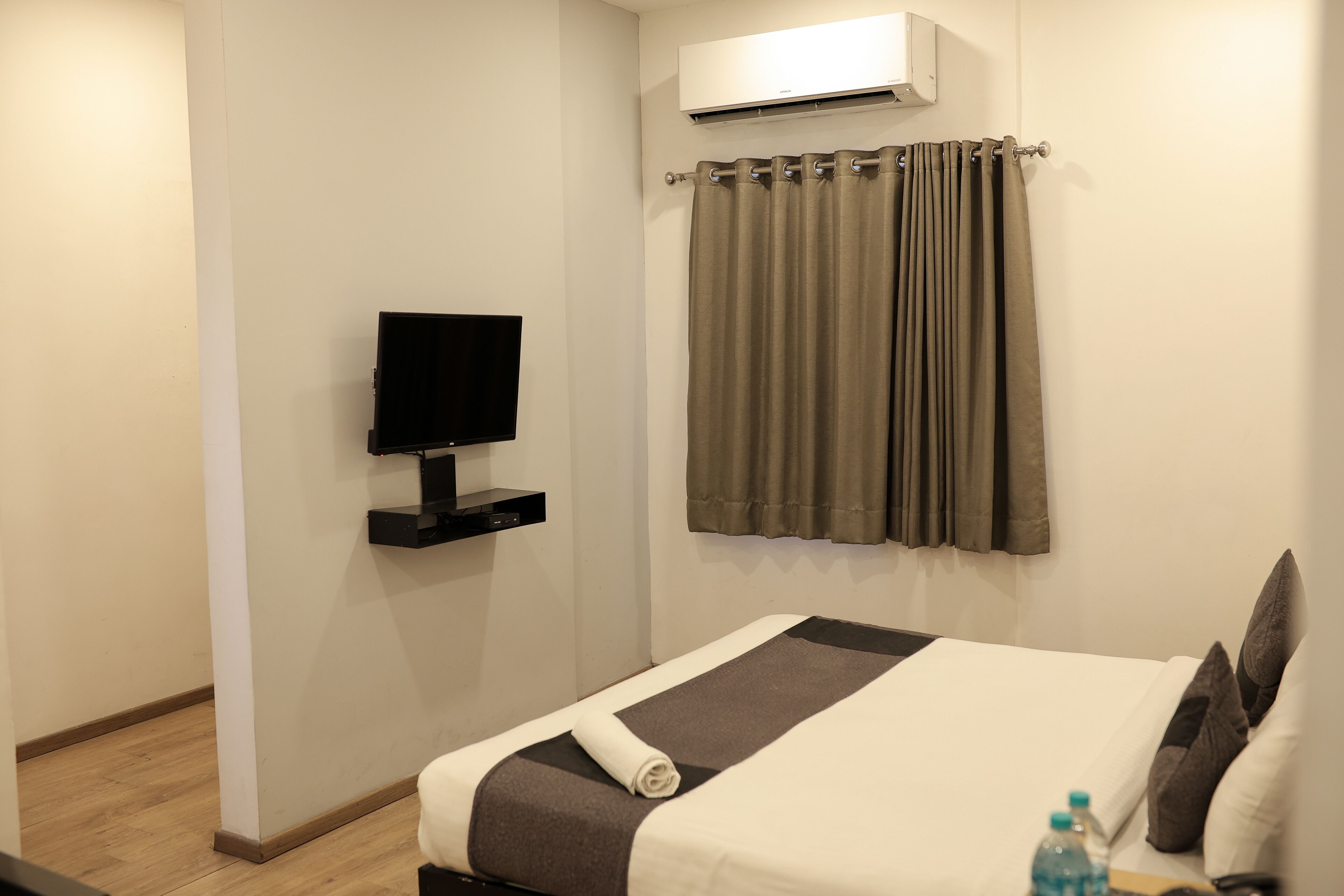 Habitación de hotel con cama, televisión de pantalla plana, aire acondicionado instalado en la pared y cortina.