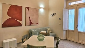 Et værelse med spisebord, stole, sofa, abstrakt vægkunst, en lampe og en dør med vinduer.