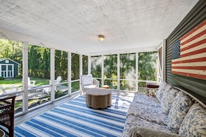 Varanda coberta com vista para um jardim, uma mesa redonda e um sofá.