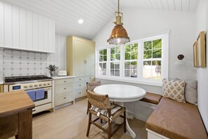 A kitchen with a stove, oven, and white cabinetry. There is a dining table with a chair and a bench with cushions. - Pro Designer Cottage, 4/10 Mile to New Circle Beach (Lakeside)