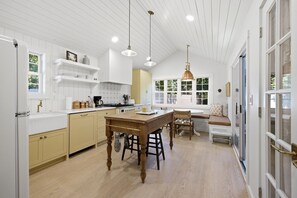A kitchen with white cabinetry, a wooden dining table, and pendant lighting.