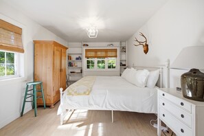 A bedroom with a bed, a wooden wardrobe, a desk, a chair, a lamp, and a wall-mounted deer head decoration. - Pro Designer Cottage, 4/10 Mile to New Circle Beach (Lakeside)
