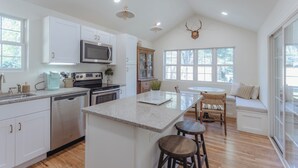A modern kitchen with white cabinets, stainless steel appliances, and a central island with stools. - Pro Designer Cottage, 4/10 Mile to New Circle Beach (Lakeside)