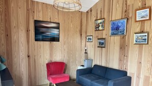 Una habitación con paneles de madera, una silla roja, un sofá azul, una mesa de centro de madera y varias obras de arte enmarcadas.