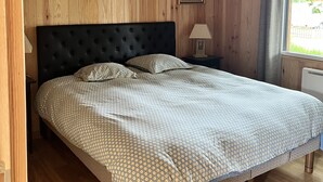 Un dormitorio con pared de paneles de madera, cabecera tapizada, colcha estampada y lámpara colgante.