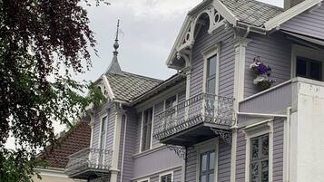 A two-story building with a balcony on the second floor, a chimney, and a small porch with potted plants.