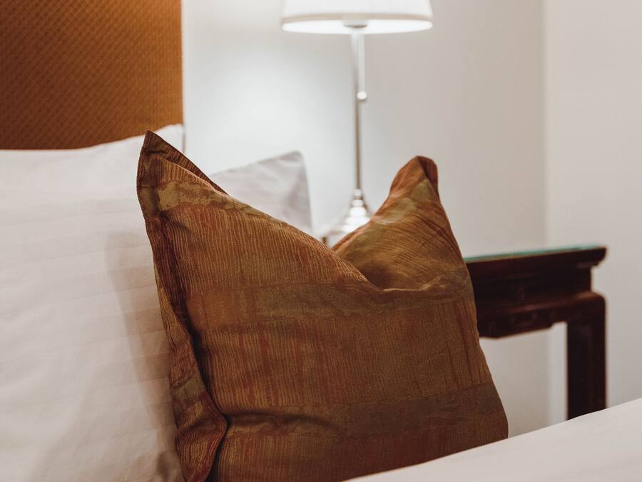 A neatly made bed with a white and brown pillow, a wooden headboard, and a bedside table with a lamp.
