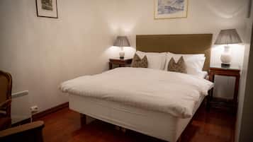 Een opgemaakt bed met witte lakens, twee nachtkastjes met lampen, en een ingelijst beeld aan de muur.