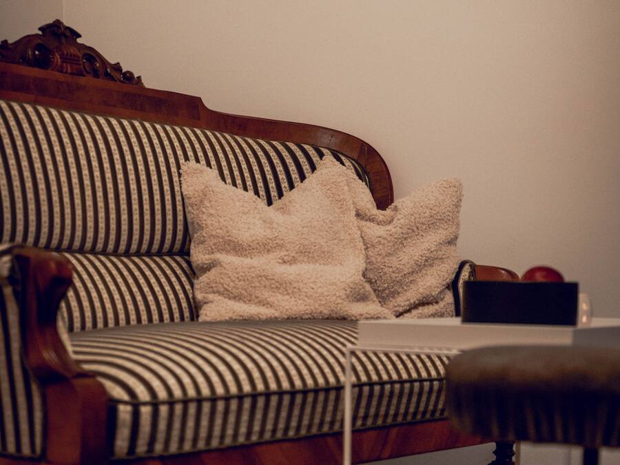 En randig soffa med träram, en vit pläd och en liten svart låda på golvet.