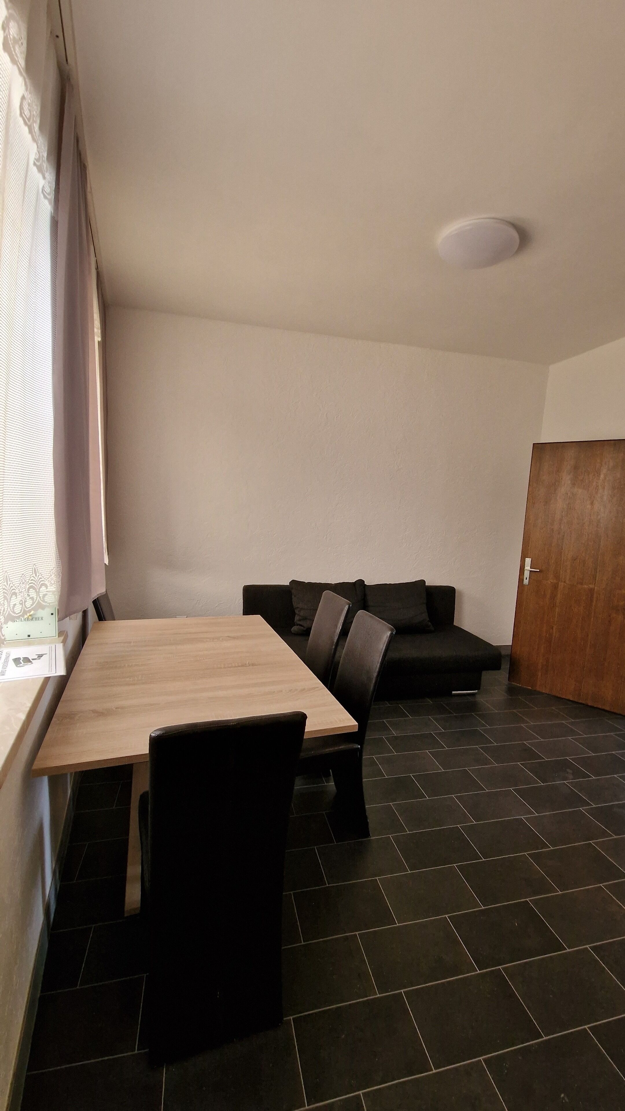Une pièce comprenant une table à manger en bois, des chaises noires, un canapé de couleur sombre et une porte en bois.