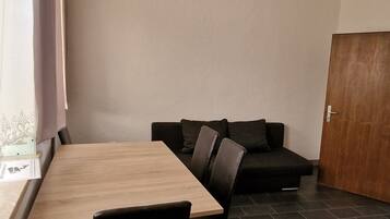 Une pièce comprenant une table à manger en bois, des chaises noires, un canapé de couleur sombre et une porte en bois.