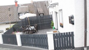 Un espace extérieur clos, avec une table et des chaises, un pot de fleurs et une boîte aux lettres fixée au mur.