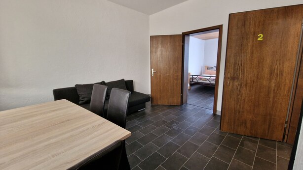 Une pièce avec une table en bois, un canapé en cuir noir et un lit dans la pièce adjacente.