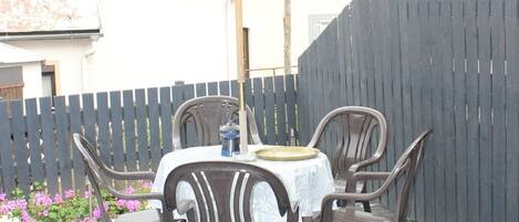 Un patio al aire libre con una mesa redonda y cuatro sillas, rodeado de un piso de ladrillo y una valla de madera.