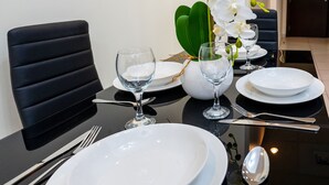 A dining table set with white plates, glasses, and cutlery, accompanied by a vase of white orchids. - Tanin - Luxurious and Contemporary Studio in JLT Cluster R (Dubai)