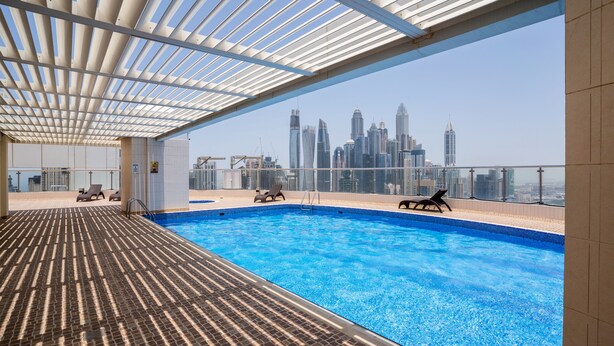 A rooftop swimming pool with a city skyline view, lounge chairs, and a covered area with a patterned floor. - Tanin - Luxurious and Contemporary Studio in JLT Cluster R (Dubai)