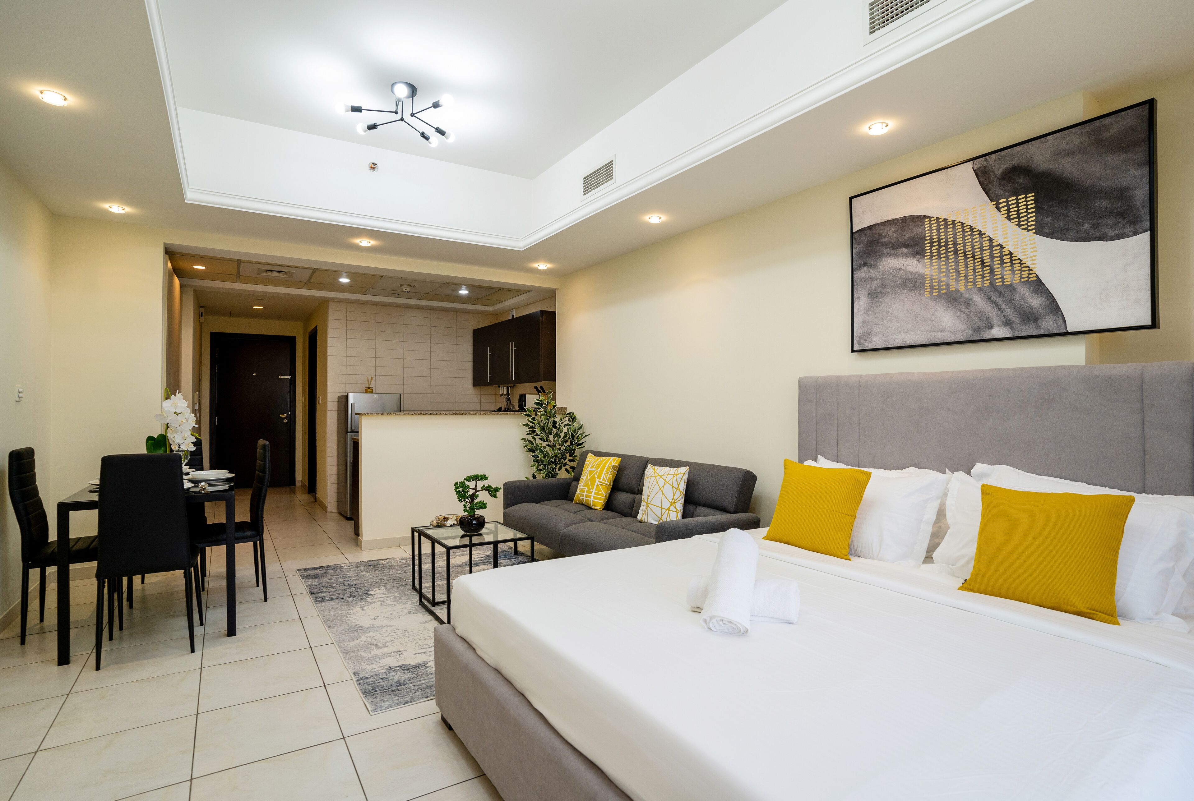 Una habitación de hotel moderna con una cama grande, un sofá, un comedor y una cocina al fondo.