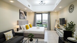A modern hotel room with a bed, a sofa, a dining table, a TV, and a large window with a city view. - Tanin - Luxurious and Contemporary Studio in JLT Cluster R (Dubai)