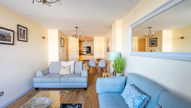 Ein Wohnzimmer mit einer Couch, einem Esstisch und einer Küche im Hintergrund.