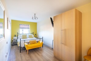 Une chambre à coucher avec un lit, un banc jaune, une armoire et un lustre.