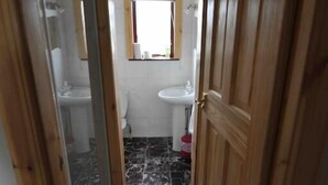 A narrow hallway with wooden doors and a marble floor leading to a bathroom with a toilet, sink, and a window above the sink. - sandwick bay guest house (Stornoway)