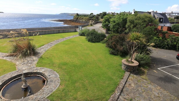 A coastal property with a stone fountain, grassy lawn, and a view of the sea. - sandwick bay guest house (Stornoway)