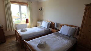 A room with two wooden beds, a wooden wardrobe, a window with curtains, a bedside table with a lamp, and a radiator. - sandwick bay guest house (Stornoway)