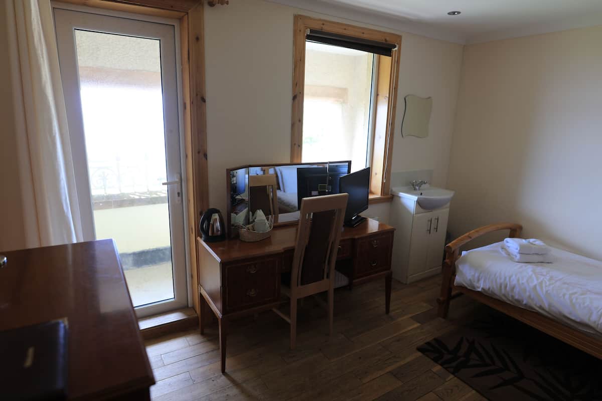 Un dormitorio con escritorio de madera, cama, ventana y baño con lavamanos y espejo.