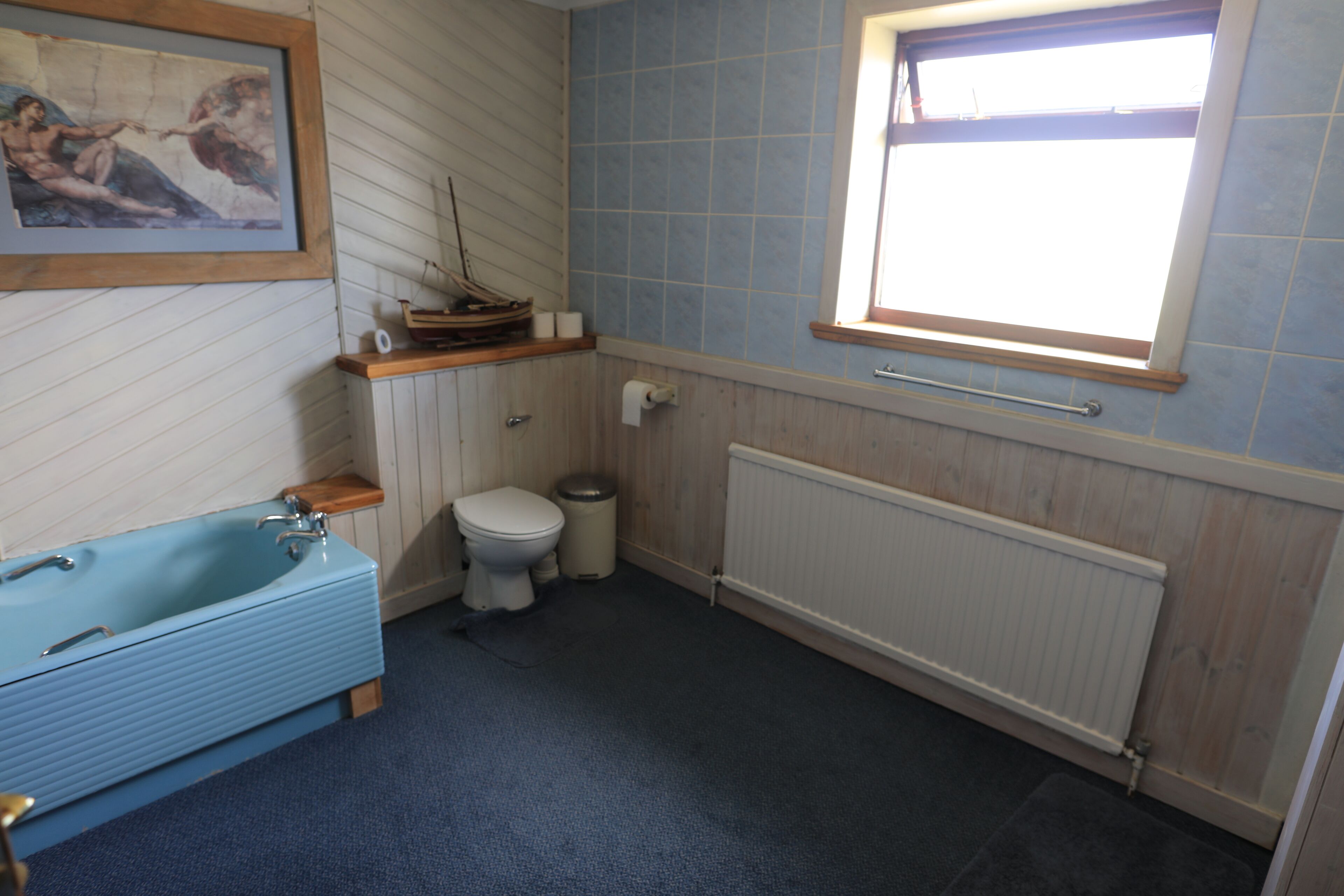 A bathroom with a blue bathtub, a toilet, a window, and a radiator.