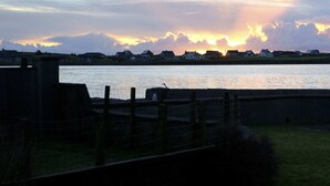 A coastal view with a sunset over the water, houses in the background, and a grassy area in the foreground. - sandwick bay guest house (Stornoway)