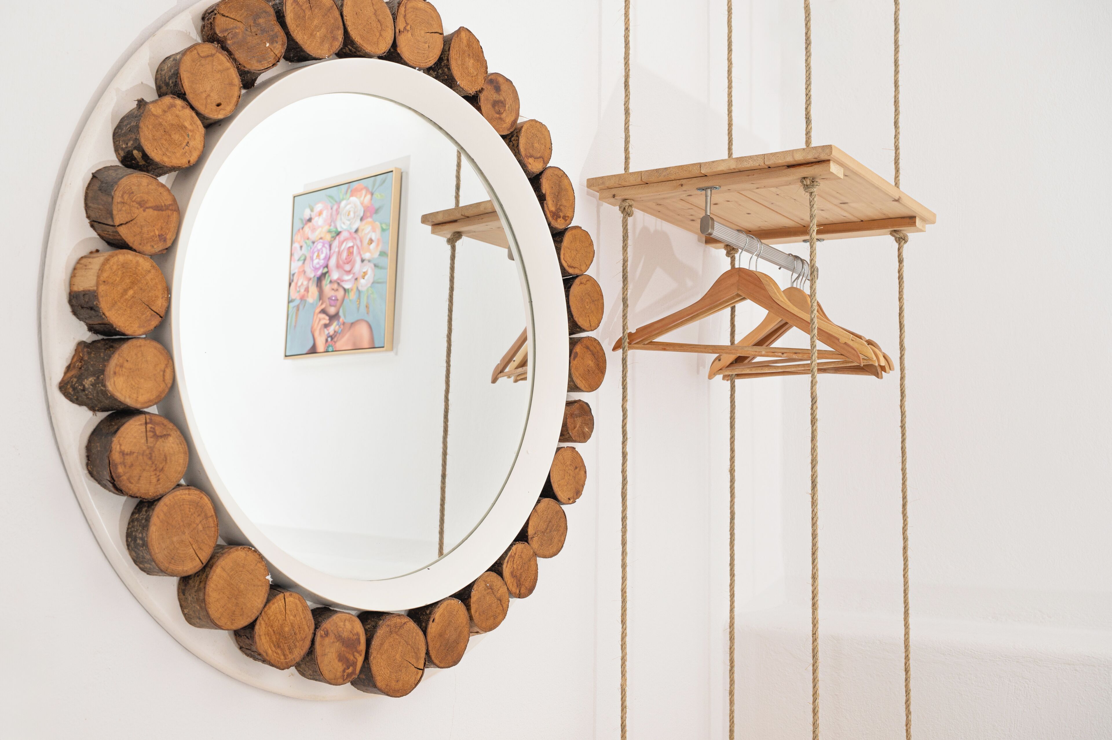 Un espejo circular rodeado por un borde de tocho de madera, con un perchero de madera y un marco de foto en la pared.