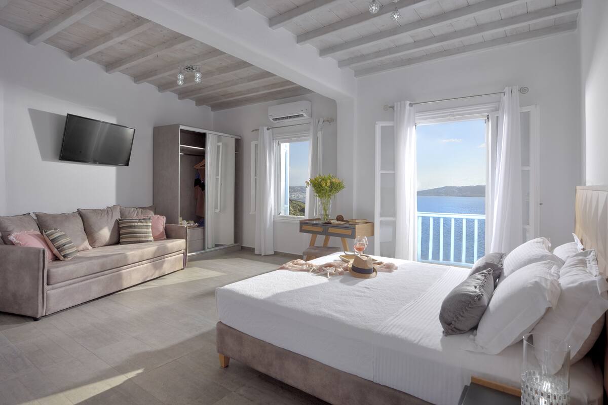 Quarto com uma cama grande, um sofá, uma TV e vista para o mar.