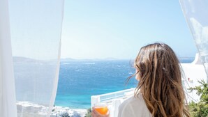 Una persona sosté un got de suc d'aranja, amb vista a la costa, edificis blancs i un cel serè.