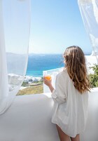 Una persona sosteniendo un vaso de jugo de naranja, con vistas a la costa, edificios blancos y cielo despejado.