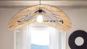 Habitació amb una finestra gran, llum penjant del sostre, decoració circular a la paret i taula de fusta amb una cadira.