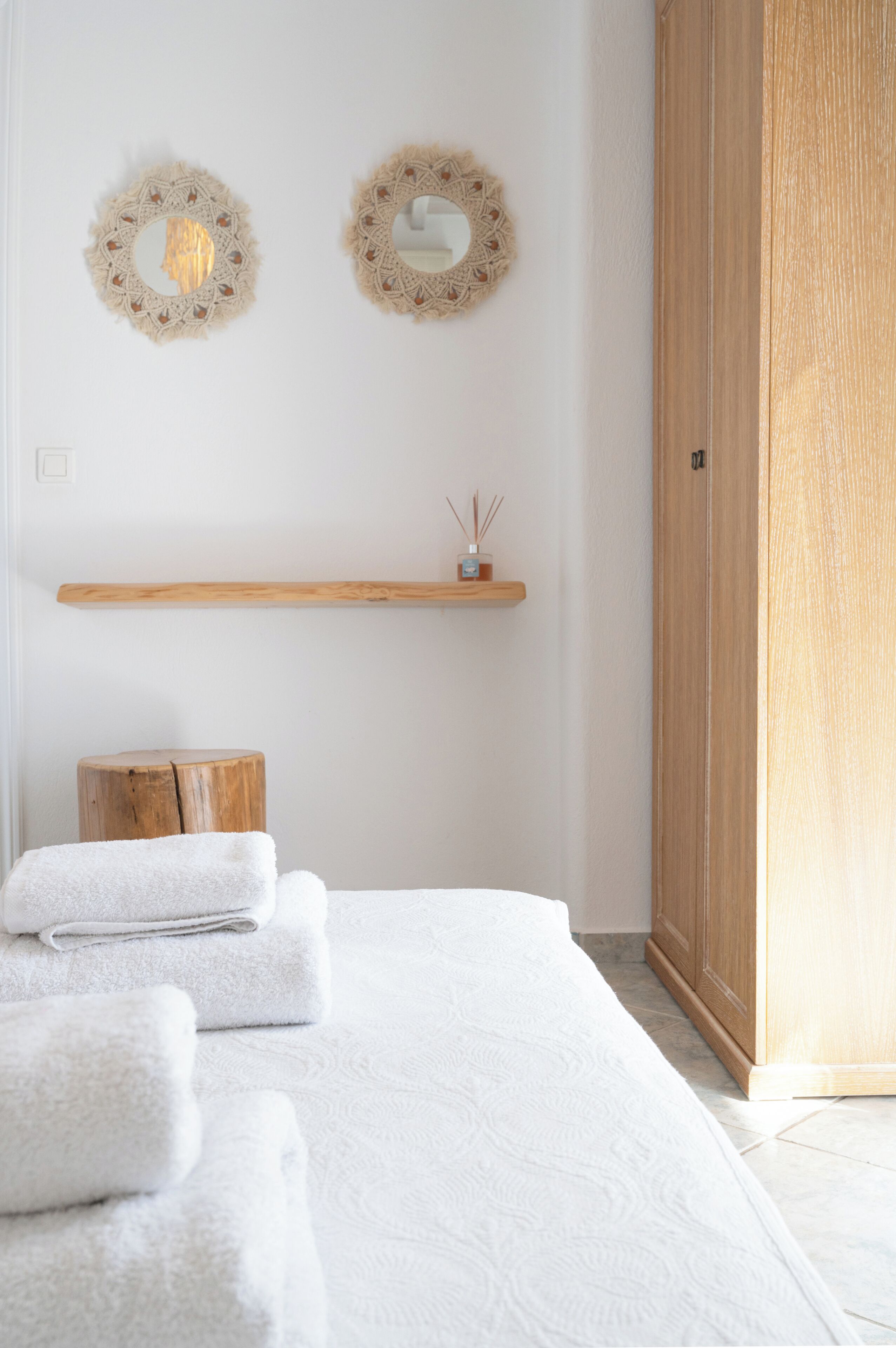 A neatly arranged bedroom with a bed, two wall mirrors, a wooden shelf with a small decorative item, and a wooden stool.